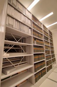 A photograph of a row of bays in a library, three of them completely filled with large books, and one of them a quarter filled. These are the pamphlets of the Congregational Library