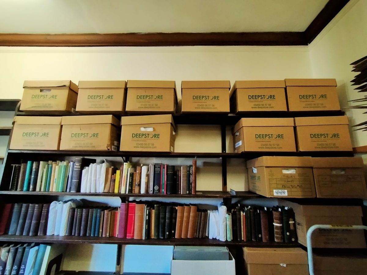 A photo of several large bankers' boxes on some bookshelves, above two rows of books.
