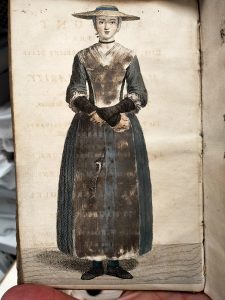 A hand-coloured female figure in a modest mid-18th century blue dress, wearing an apron and hat and elbow-length mittens